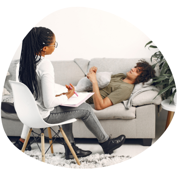 A person lying on a couch while a therapist takes notes during a session